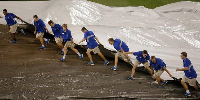 Members of the grounds crew pull the tarp on the field during a rain delay in the 10th inning of a baseball game between the Kansas City Royals and the Cleveland Indians Sunday, Aug. 31, 2014, in Kansas City, Mo. (AP Photo/Charlie Riedel)