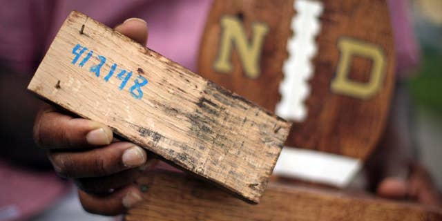 FILE - In this Aug. 14, 2015 file photo, Larry Stephney holds a piece of wood with the number 412148 written on it that is from a product made while he was an inmate at a privately run prison in Nashville, Tenn. The number refers to a section of Tennessee code that makes it illegal for jail officials to require an inmate to perform labor that results in the official’s personal gain. Stephney says inmates were required to build plaques, birdhouses, dog beds and cornhole games for officials who sold the items through an online business and at a local flea market. Two Nashville jail employees and one former employee are charged with official misconduct, accused of pocketing money from the sale of inmate-made wooden plaques and games. (AP Photo/Mark Humphrey, File)