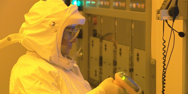 A manufacturing technician, wearing a protective suit to keep dust particles out of a clean room, uses a scanner to start production of CPU wafers inside an Intel chip factory in Chandler, Ariz.