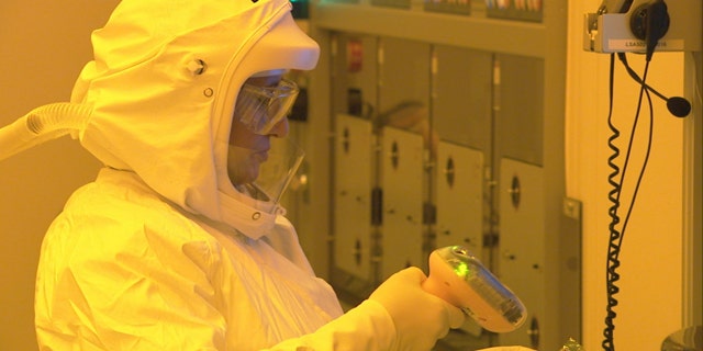 A manufacturing technician, wearing a protective suit to keep dust particles out of a clean room, uses a scanner to start production of CPU wafers inside an Intel chip factory in Chandler, Ariz.