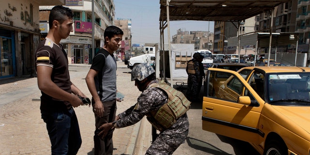 July 15, 2012: An Iraqi police officer searches people at a checkpoint in central Baghdad, Iraq.