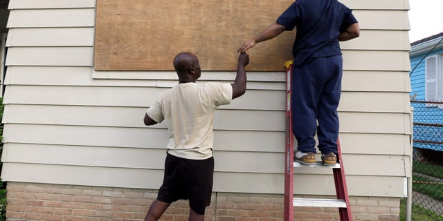 Aug. 28, 2012: Stacey Davis, left, hands a screw to his son as they board up windows on their home before Hurricane Isaac hits in New Orleans.