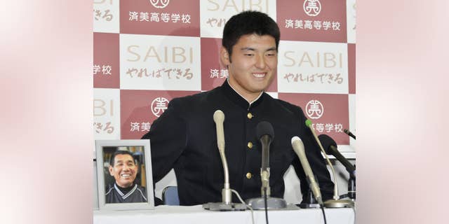 Japan's high school pitching star Tomohiro Anraku smiles next to a photo of his baseball team head coach Masanori Joko who died in September during a news conference at Saibi High School in Matsuyama, western Japan, Thursday, Oct. 23, 2014, after he was chosen first overall in Nippon Professional Baseball's amateur draft and was headed to the former team of New York Yankees pitcher Masahiro Tanaka. The Yakult Swallows and Rakuten Eagles selected Anraku, whose fastball has been clocked as high as 97 mph (156 kph), with the first and second picks respectively, and the Eagles won a lottery for the highly touted 17-year-old right-hander. (AP Photo/Kyodo News) JAPAN OUT, CREDIT MANDATORY