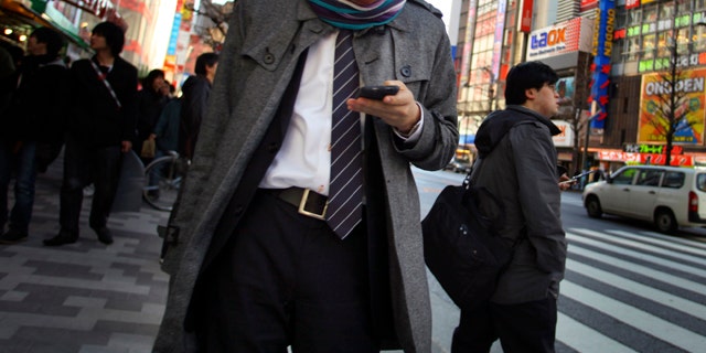 A young man uses a cell phone in a street in Tokyo Friday, March 4, 2011. Japan is engaging in soul-searching after police arrested a 19-year-old accused of cheating on a prestigious university's entrance examination by using his mobile phone to post questions on a popular online forum and get outside help.