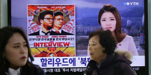 FILE - In this Dec. 22, 2014 file photo, people walk past a TV screen showing a poster of Sony Pictures Entertainment's 'The Interview' in a news report at the Seoul Railway Station in Seoul, South Korea. (AP Photo/Ahn Young-joon, File)