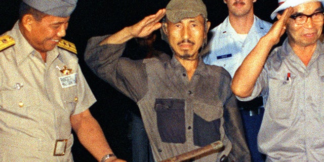 FILE 1974: Hiroo Onoda, center, salutes after handing over his military sword on Lubang Island, Philippines, when he comes out of hiding in the jungle.