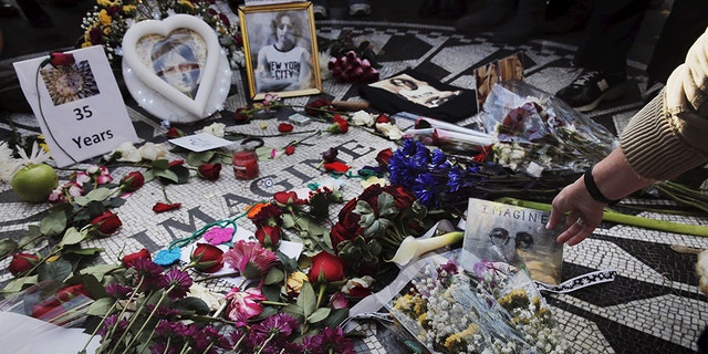 A woman sets a photograph down as she joins fans of former Beatle John Lennon who have gathered at the Imagine mosaic in the Strawberry Fields section of New York's Central Park to mark the 35th anniversary of his death, in New York on Dec. 8, 2015.