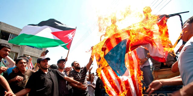 Demonstrators burn a U.S. flag as a Jordanian flag is held aloft by a protester in Amman, Jordan, Friday July 22, 2011. Protesters denounce what they call U.S. interference in their government's policies, demanded democratic reforms sweeping the Arab region, and for Prime Minister Marouf al-Bakhit to step down.
