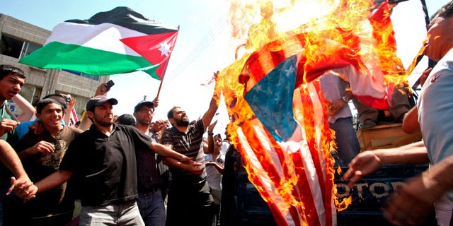 Demonstrators burn a U.S. flag as a Jordanian flag is held aloft by a protester in Amman, Jordan, Friday July 22, 2011. Protesters denounce what they call U.S. interference in their government's policies, demanded democratic reforms sweeping the Arab region, and for Prime Minister Marouf al-Bakhit to step down.