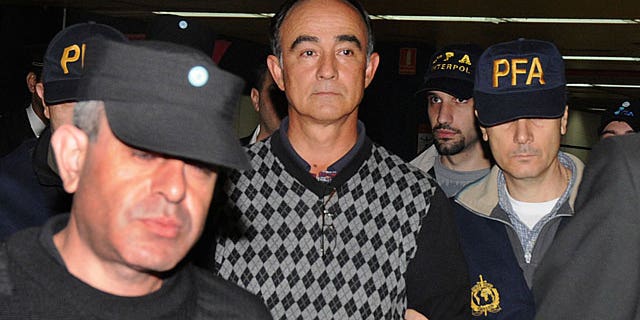 May 6: Police officers escort Argentine airline pilot Julio Alberto Poch upon his arrival at Buenos Aires airport after being extradited from Spain. (AP)