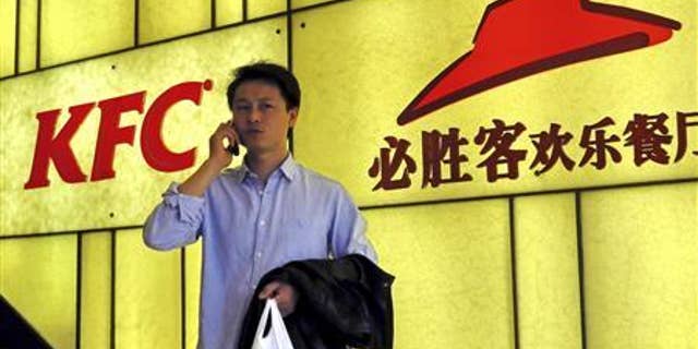 A man talks on his mobile phone in front of the logos of KFC and Pizza Hut, both restaurants under Yum Brands, in Shanghai, March 6, 2013. REUTERS/China Daily