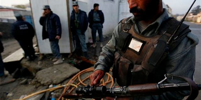 An Afghan policeman with blood in his hand and badge adjusts his gun as others take cover close to the site of a attack in Kabul, Afghanistan on Wednesday, Oct. 28, 2009. Gunmen with automatic weapons and suicide vests stormed a guest house used by U.N. staff in the heart of the Afghan capital early Wednesday, officials said. A Taliban spokesman claimed responsibility, saying it was meant as an assault on the upcoming presidential election. (AP Photo/ Gemunu Amarasinghe)