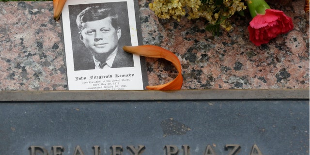 A photo of JKF and flowers lay on a plaque at Dealey Plaza in Dallas, Thursday, Nov. 21, 2013. Loose gatherings of the curious and conspiracy-minded at Dallasâ Dealey Plaza have marked past anniversaries of the assassination of President John F. Kennedy. But for the 50th anniversary, the city of Dallas has planned a solemn ceremony Friday in the plaza he was passing through when shots rang out. There will be brief remarks by the mayor and the tolling of church bells. (AP Photo/LM Otero)