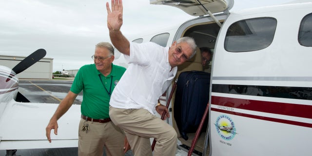 In this photo provided by the Florida Keys News Bureau, Key West Mayor Craig Cates, right, waves goodbye as he boards a chartered aircraft at Key West International Airport Monday, Dec. 30, 2013, that flew to Havana, Cuba. The trip was the first legal commercial passenger flight from Key West to Cuba in more than 50 years and carried passengers who will remain until Jan. 3, 2014. It was organized by the Florida Keys Tropical Research Ecological Exchange Institute under a people-to-people cultural exchange license. Cates accompanied the passengers but did not stay in Cuba and returned to Key West. At left is Monroe County Airports Director Peter Horton. (AP Photo/Florida Keys News Bureau)