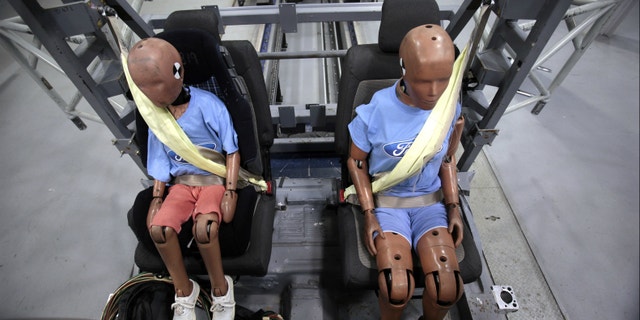 Two Ford Motor Co. crash test dummies sit strapped in a Servo Sled Crash Simulator with seat belt air bags.