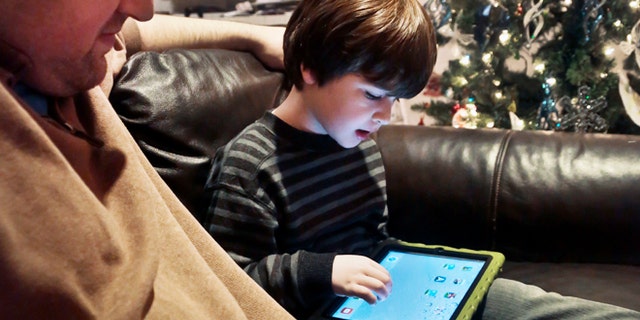 Adam Cohen watches as his son Marc, 5, uses a tablet at their home in New York Dec. 3, 2013.