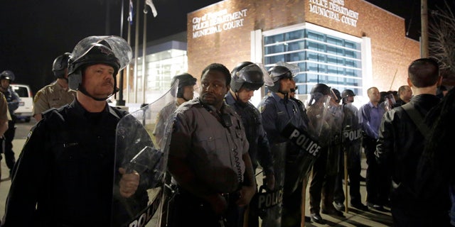 Police form a line outside the Ferguson Police Department as people demonstrate nearby Wednesday, March 11, 2015, in Ferguson, Mo. Earlier in the day, the resignation of Ferguson police chief Thomas Jackson was announced in the wake of a scathing Justice Department report prompted by the fatal shooting of an unarmed black 18-year-old by a white police officer. (AP Photo/Jeff Roberson)