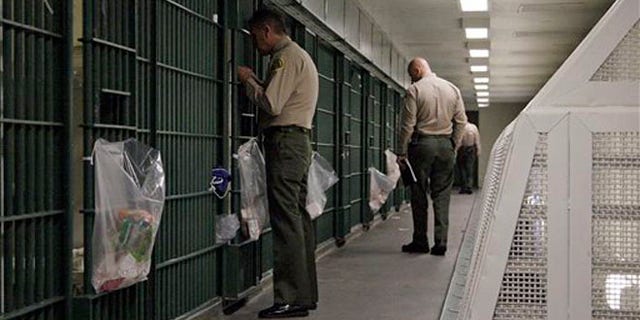 FILE - In this Oct. 3, 2012, file photo, Los Angeles County Sheriff's deputies inspect a cell block at the Men's Central Jail in downtown Los Angeles. A new federal civil rights indictment alleges that two Los Angeles County sheriff's deputies beat a handcuffed prisoner at the Men's Central Jail. The four-count indictment returned by a grand jury late Thursday Feb. 6, 2014, follows earlier indictments of 18 current and former Los Angeles County deputies on corruption and civil rights offenses. (AP Photo/Reed Saxon, File)