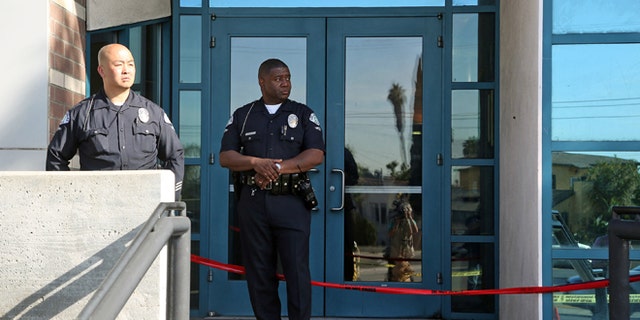 Los Angeles police officers stand outside the West Traffic Division station Tuesday, April 8, 2014, after an officer was shot and wounded inside the station Monday evening. A gunman who opened fire inside the police station, hitting one officer several times, was hospitalized early Tuesday in critical condition after he was wounded in the ensuing gunbattle, authorities said. (AP Photo/Nick Ut )