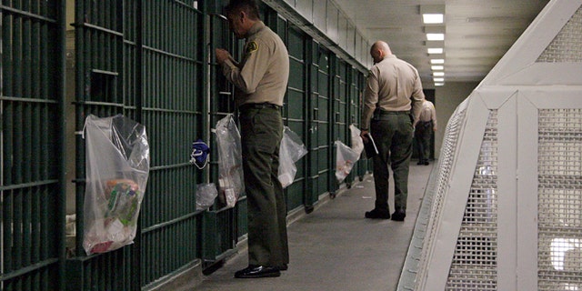 FILE - In this Oct. 3, 2012, file photo, Los Angeles County Sheriff's deputies inspect a cell block at the Men's Central Jail in downtown Los Angeles. Federal officials say 18 current and former Los Angeles County sheriff's deputies saw themselves as being "above the law," engaging in corruption and civil rights abuses that included beating inmates and visitors, falsifying reports, and trying to block an FBI probe of the nation's largest jail system. (AP Photo/Reed Saxon, File)