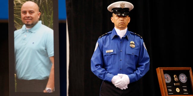 A TSA officer standS in front of a portrait of slain TSA officer Gerardo Hernandez during his public memorial at the Los Angeles Sports Arena, Tuesday, Nov. 12, 2013.