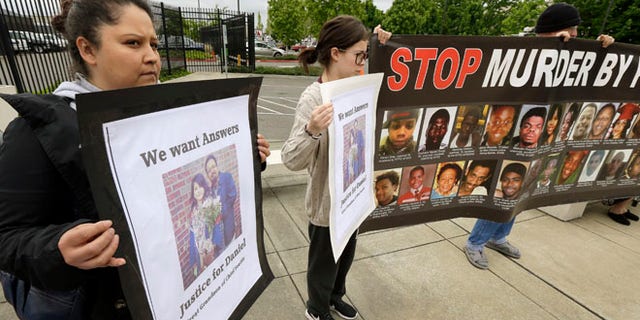 Lanna Covarrubias, left, the sister of Daniel Covarrubias, holds a sign Monday, May 11, 2015, as she stands with supporters outside police headquarters in Lakewood, Wash. The interim police chief in Lakewood says officers shot and killed Daniel Covarrubias in a lumber yard last month because he pointed a cell phone at them as though it were a gun. (AP Photo/Ted S. Warren)