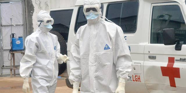 Health workers wearing protective gear wait to carry the body of a person suspected to have died from Ebola, in Monrovia, Liberia, Monday Oct. 13, 2014. (AP Photo/Abbas Dulleh)