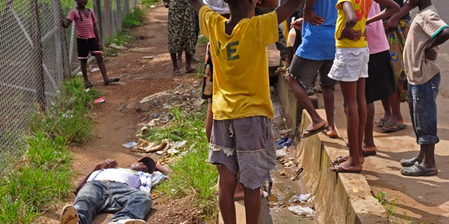 August 19, 2014: Children surround a man, left, who fell down while walking on a street suspected of having contracted the Ebola virus in the city of Monrovia, Liberia. The World Health Organization says the outbreak has killed more than 1,200 people, while authorities struggle to contain its spread and treat the sick. (AP Photo/Abbas Dulleh)