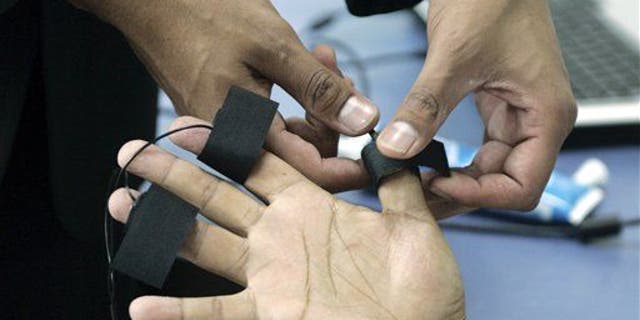 A polygraph examiner applies electrodes on the fingers of a subject.