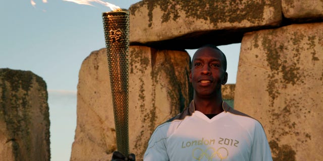 July 12, 2012: U.S. Olympian sprinter Michael Johnson poses for photographers holding the Olympic Flame at Stonehenge, England.