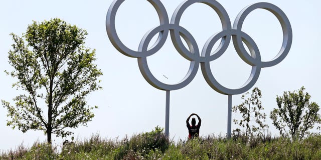 Volunteer Abby Idowu, of London, stretches under the Olympic rings while being photographed by friends on the other side of a hill at Olympic Park prior to the 2012 Summer Olympics, Thursday, July 26, 2012, in London. The opening ceremonies for the games will be held Friday, July 27. (AP Photo/Charles Krupa)