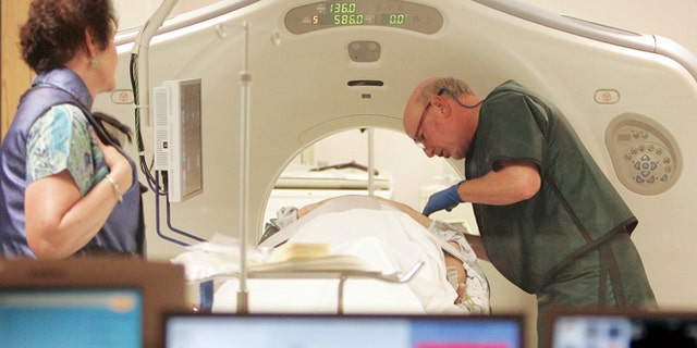 FILE - In this June 3, 2010, file photo, Dr. Steven Birnbaum works with a patient in a CT scanner at Southern New Hampshire Medical Center in Nashua, N.H. A national study suggests the world's top cancer killer isn't always as deadly as doctors once thought, finding that more than 18 percent of lung cancers detected in screening scans are likely so slow growing that theyâd never cause problems. But the provocative results are unlikely to change how doctors treat lung cancer. (AP Photo/Jim Cole, File)