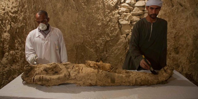 Egyptian excavation workers restore a mummy in a newly discovered tomb on Luxor's West Bank in Luxor Saturday.
