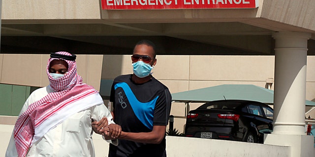A man, wearing a surgical mask as a precautionary measure against the novel coronavirus, helps a friend who has the common flu near a hospital in Khobar city in Dammam May 23, 2013.