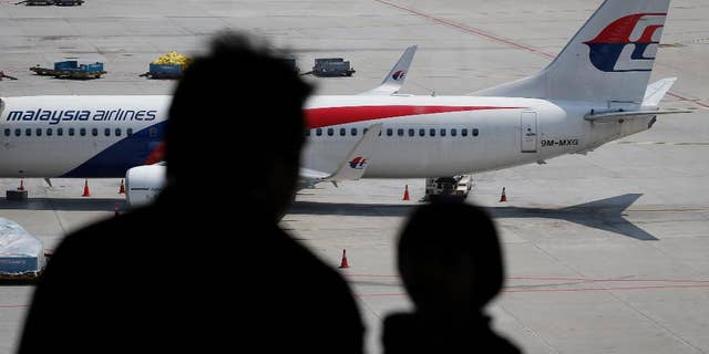 In this Friday, Feb. 27, 2015 photos, visitors look out from a viewing gallery as a Malaysia Airlines plane sits in the tarmac at the Kuala Lumpur International Airport (KLIA) in Sepang, Malaysia. After a year of unprecedented calamity for the Southeast Asian carrier, Malaysia Airlines is aiming to return to profitability by 2017 with a drastic $1.7 billion overhaul that includes cutting nearly a third of its staff. (AP Photo/Vincent Thian)