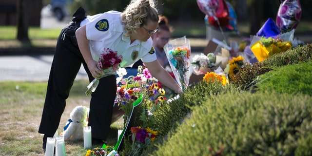A security guard working at the Cascade Mall places flowers at a makeshift memorial on Sunday, Sept. 25, 2016, in Burlington, Wash., to the five victims killed in a shooting at the mall on Friday. The 20-year-old man suspected of killing the five people with a rifle at a Macy's makeup counter had a string of run-ins with the law in recent years, including charges he assaulted his stepfather. (AP Photo/Stephen Brashear)