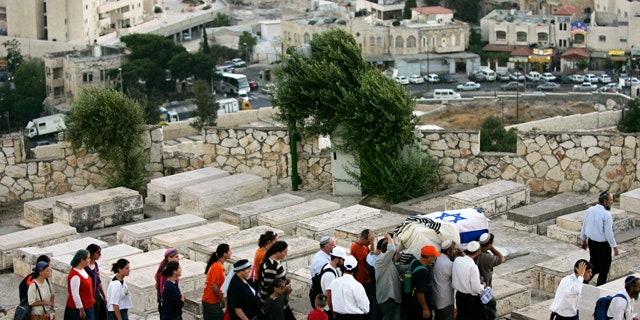 Israeli men carry a coffin wrapped in an Israeli flag and a prayer shawl as women follow during a reburial ceremony for fifteen Jewish settlers at the Mt. of Olives cemetery in Jerusalem. A Jewish group is using 21st-century technology to map every tombstone in the ancient cemetery on the Mount of Olives, a sprawling, politically sensitive necropolis of 150,000 graves stretching back three millennia.