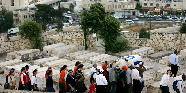 Israeli men carry a coffin wrapped in an Israeli flag and a prayer shawl as women follow during a reburial ceremony for fifteen Jewish settlers at the Mt. of Olives cemetery in Jerusalem. A Jewish group is using 21st-century technology to map every tombstone in the ancient cemetery on the Mount of Olives, a sprawling, politically sensitive necropolis of 150,000 graves stretching back three millennia.