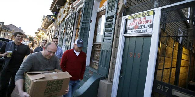 FILE - In this Jan. 18, 2015 photo, men walk past a sign encouraging people to walk in large groups, in the French Quarter of New Orleans. A spike in violent crime in the French Quarter is unsettling residents and comes just as New Orleans prepares to host crowds of tourists for Mardi Gras. Mardi Gras falls on Feb. 17 this year. (AP Photo/Gerald Herbert, File)