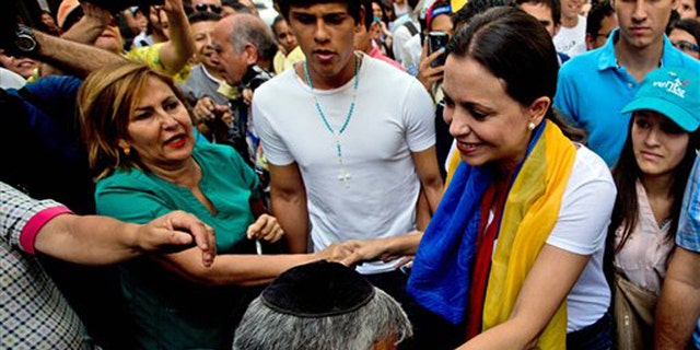 A man kisses the hand of leading opposition politician Maria Corina Machado as she arrives for a rally in Caracas, Venezuela, Wednesday, March 26, 2014. The head of Venezuela's congress, Diosdado Cabello, said Monday that Machado, who was stripped of her parliament seat, violated the constitution by addressing the Organization of American States last week at the invitation of Panama, which ceded its seat at the Washington-based group group so she could provide regional diplomats with a firsthand account of the unrest. (AP Photo/Fernando Llano)