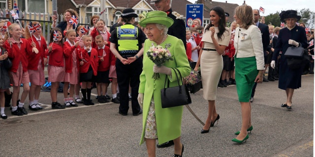 Britain's Queen Elizabeth II and Meghan, the Duchess of Sussex, third right, are welcomed by well-wishers after arriving by Royal Train at Runcorn Station, northwest England.