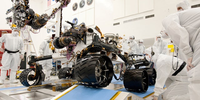 Technicians working on the new Mars rover, Curiosity. Nine months before Curiosity's scheduled launch, the space agency says the mission has burned through its reserves and needs an extra $82 million to complete testing before liftoff.