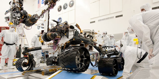 Technicians working on the new Mars rover, Curiosity. Nine months before Curiosity's scheduled launch, the space agency says the mission has burned through its reserves and needs an extra $82 million to complete testing before liftoff.