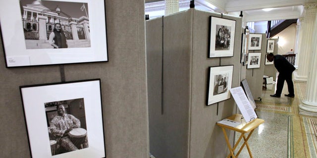 In this Thursday, Nov. 17, 2016 photo Teddy Chery, of Medford, Mass., right, pauses to examine an image that forms part of an exhibit by photographer Mark Chester at the Statehouse, in Boston. Cape Cod-based Chester has produced a collection of photographs of immigrants from all over the world called The Bay State: A Multicultural Landscape - Photographs of New Americans. (AP Photo/Steven Senne)