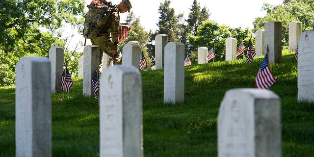 A member of the Army 3d U.S. Infantry Regiment, The Old Guard, places a flag at the headstone of fallen military member during its annual Flags In ceremony at Arlington National Cemetery, Thursday, May 24, 2018, in Arlington, Va. (AP Photo/Cliff Owen)
