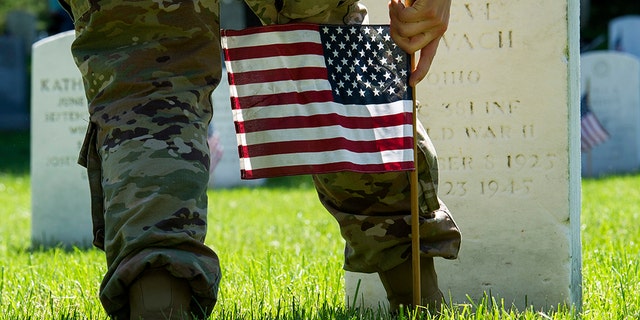 A member of the Army 3d U.S. Infantry Regiment, The Old Guard, places a flag at the headstone of fallen military member during its annual Flags In ceremony at Arlington National Cemetery, Thursday, May 24, 2018, in Arlington, Va. (AP Photo/Cliff Owen)