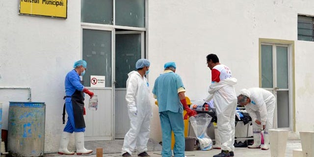 Forensic workers suit up as they continue the autopsies of 11 slain family members at a morgue inside the cemetery of the city of Tehuacan, Mexico, Saturday, June 11, 2016. Five women, four men and two girls of the same family were found shot to death on Thursday in the town of San Jose el Mirador in Puebla's state municipality of Coxcatlan, in central Mexico. The prime suspect in the brutal slaying is a man who allegedly sought revenge after one of the victims reported that he raped her and he was jailed, a Mexican law enforcement official said Saturday. (AP Photo/Pablo Spencer)