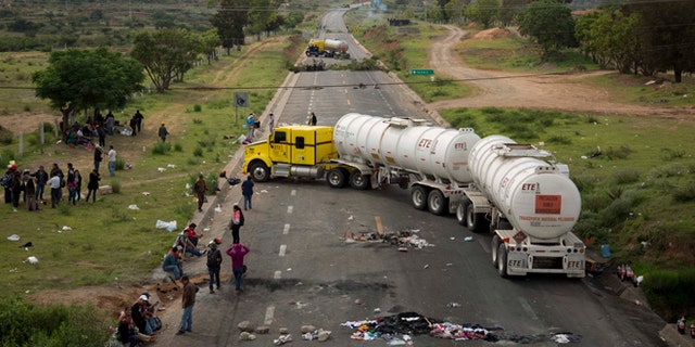 Protesters stand beside trucks blocking the highway in the state of Oaxaca, near the town of Nochixtlan, Mexico, Monday, June 20, 2016. Mexican police say few teachers were involved in violence at a weekend highway protest in the southern state of Oaxaca in which six people died. The teachers are protesting against plans to overhaul the country's education system which include federally mandated teacher evaluations. (AP Photo/Eduardo Verdugo)