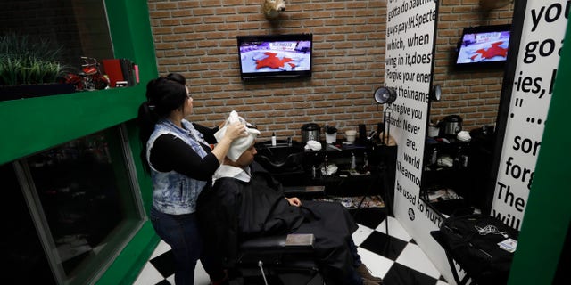 Paula Noriega, left, looks up at a screen displaying news of the elections in the United States as she dries the hair of Alan Maldonado at a barber shop Tuesday, Nov. 8, 2016, in Tijuana, Mexico. (AP Photo/Gregory Bull)
