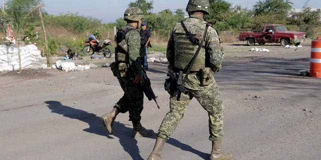Mexican army soldiers walk at the entrance into the town of La Ruana a day after a clash between two rival "self-defense" groups outside of the town, in the state of Guerrero, Mexico, Wednesday Dec. 17, 2014. According to federal authorities, both groups fought at a barricade at the entrance to the community resulting in several dead on both sides. (AP Photo/Gustavo Aguado)